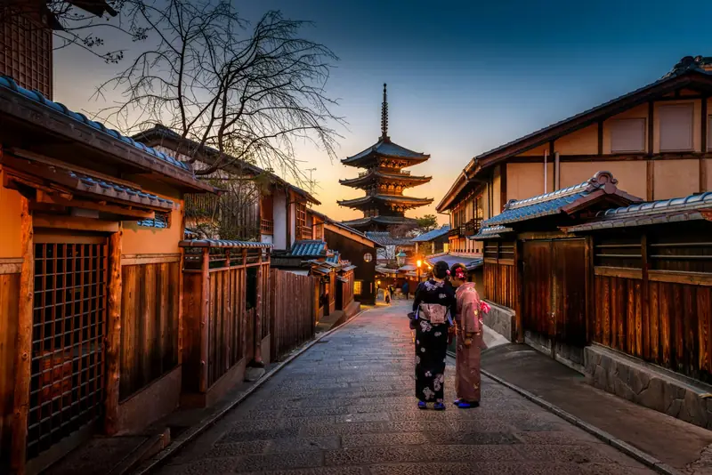 Two women in kimono on a stone-paved street below Yasaka Pagoda at dusk in Higashiyama, Kyoto